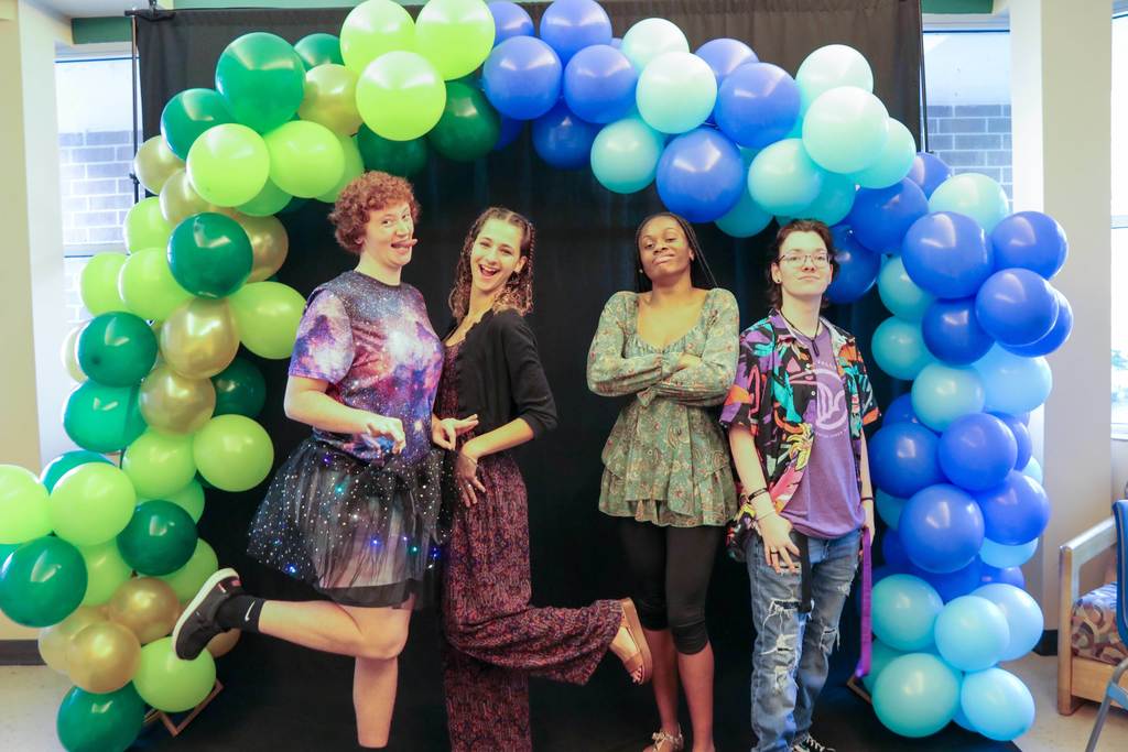Four student dressed in colorful clothing as they smile for their photo at the photo op booth. 