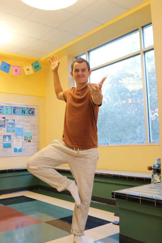 A high schooler is wearing tan pants with a brown shirt resembling the earth poses with one foot for the photo inside the Pope hallway.