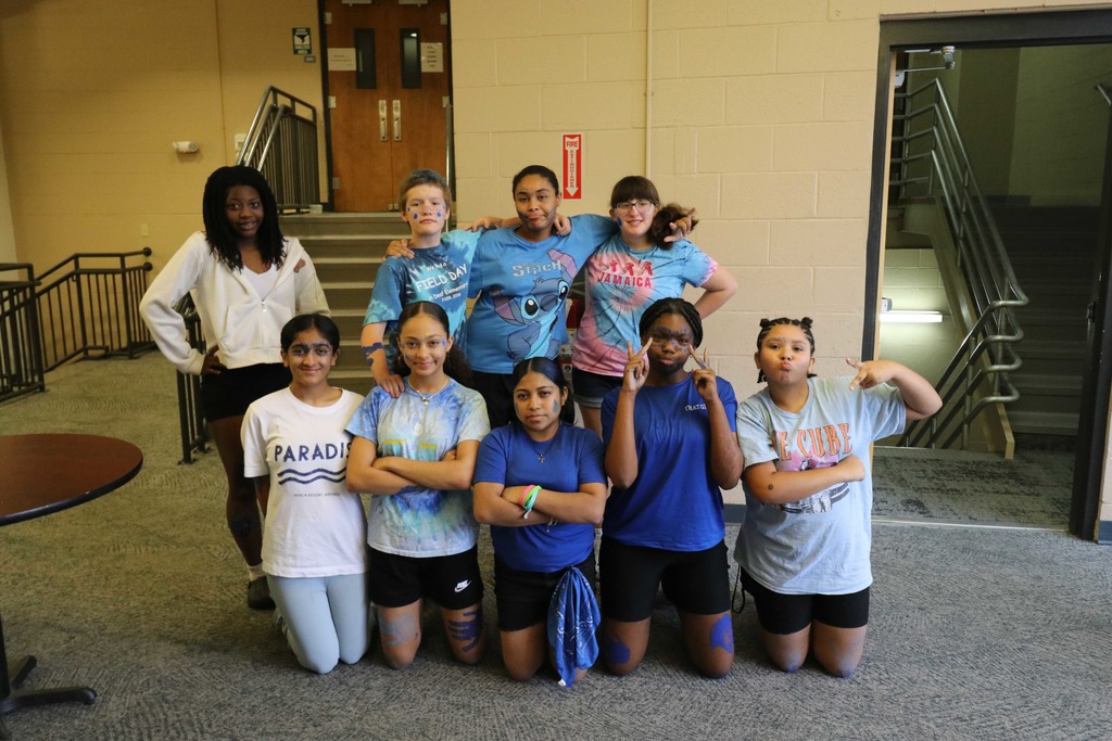 A group of middle schoolers are dressed in white and blue resembling water smile as a group for a photo. 