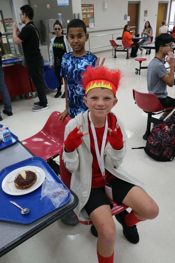 A student is wearing red gloves and a red fire hat smiling for his photo inside the cafeteria. 