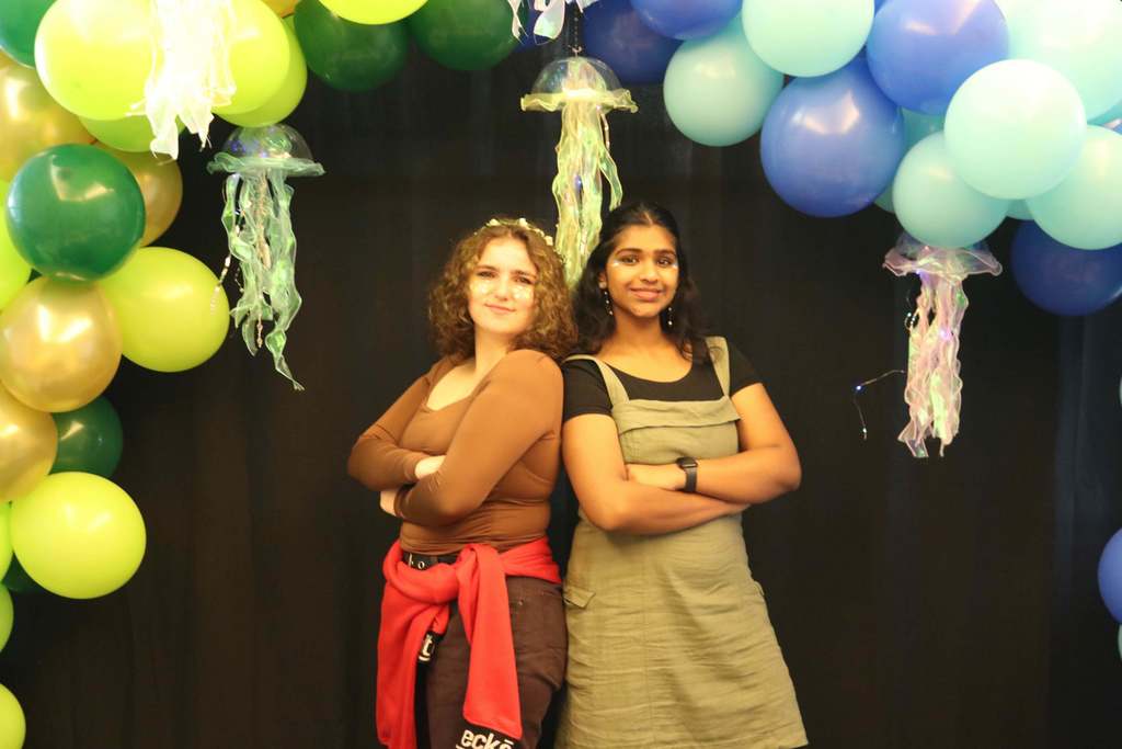 Two high schoolers are dressed for earth with their brown and olive green colors pose with their arms crossed for the photo. 