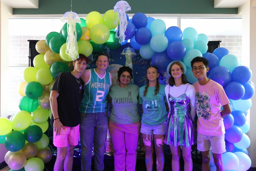 Group of juniors smiling with the blue light shining on their clothing inside a classroom. 
