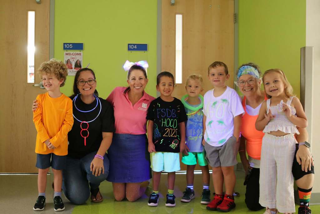 Group of elementary students and staff members smiling for their photo wearing neon color clothing. 