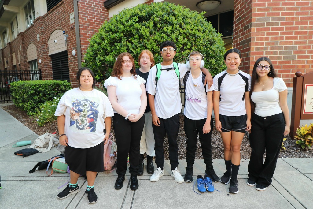 Group of students wearing white shirts and black bottoms smiling for their photo outside of Pope. 