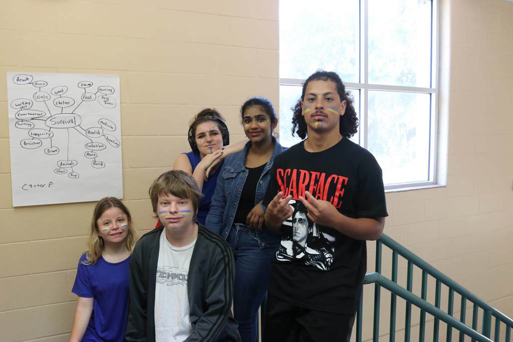 Group of students smiling for their photo with yellow and blue face paining on their face in the hallway. 