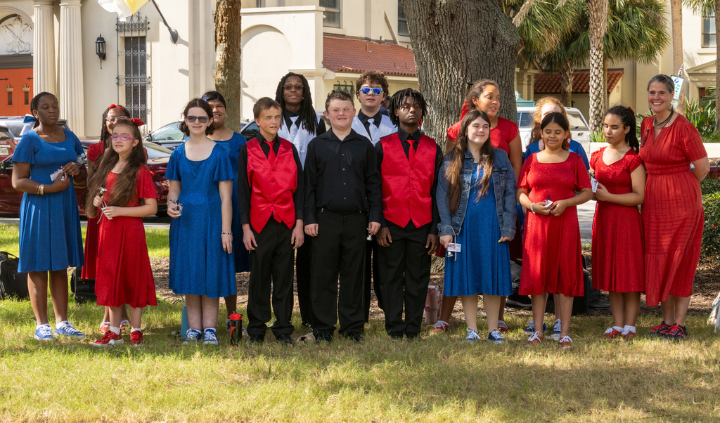 A group photo of the students wearing variety of colors between red, blue and white smiling with President Snow outside of the plaza downtown St. Augustine. 