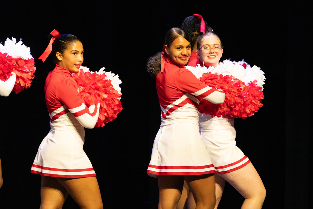 FSDB cheerleaders on stage in Kirk smiling and dancing with their red and white pom poms. 