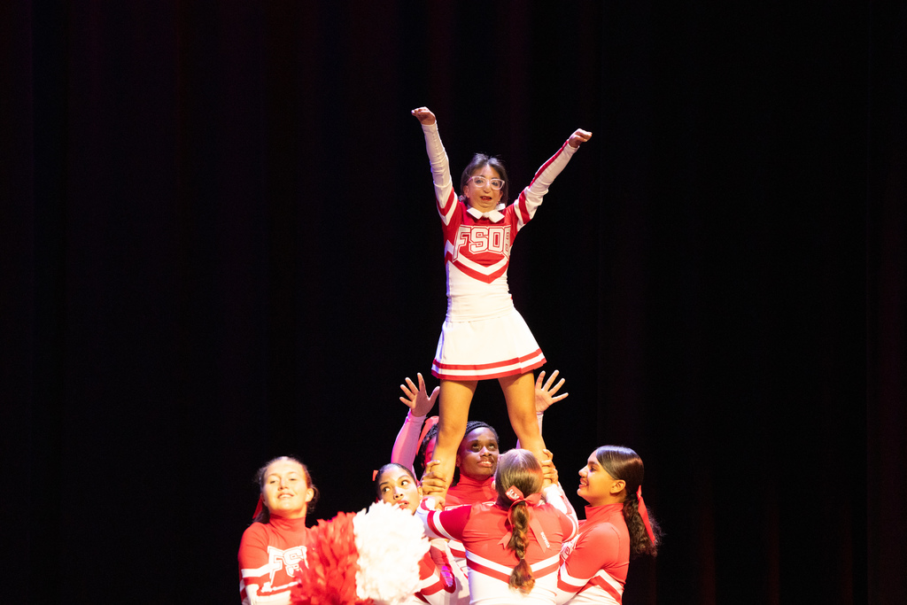 FSDB cheerleaders doing a stunt with the flyer who is holding her arms up on stage in Kirk. 