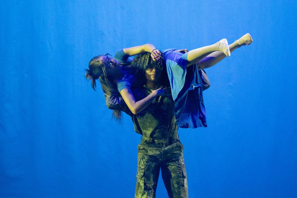 Two dance troupe students dressed in camo and blue relating to the Avatar theme dance on stage in Kirk. The boy is holding the girl on her shoulders. 