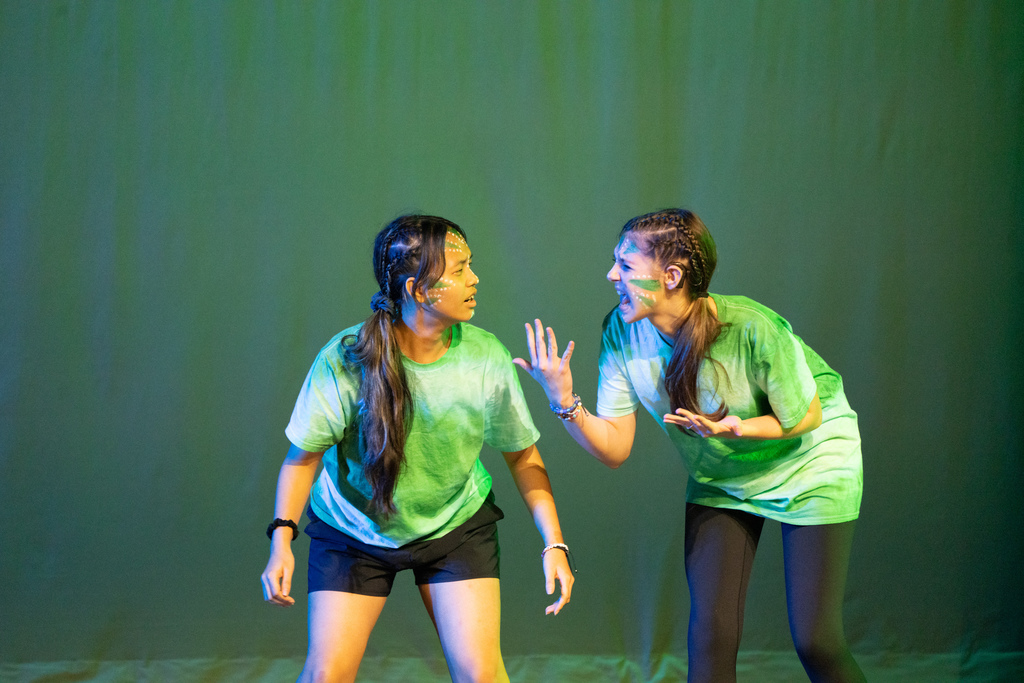 Two students wearing green with green face painting and performing on stage in Kirk. 