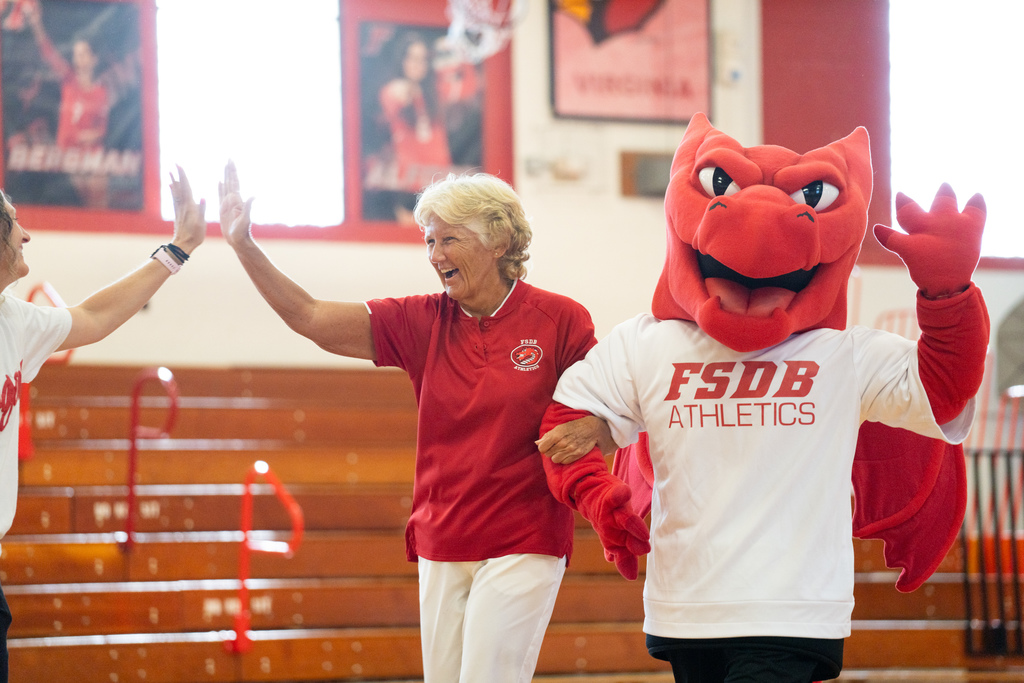 A former staff member hold arms with Samy the Dragon inside Settles Gym. 