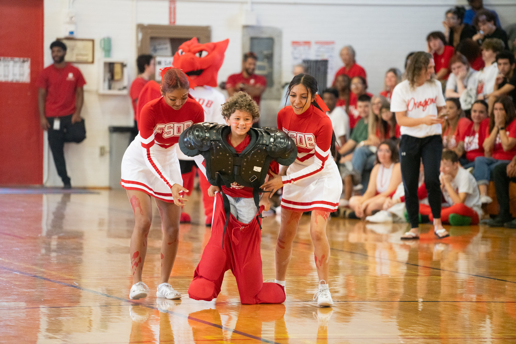 Two FSDB cheerleaders help an elementary school student dressed up in football gear during a race game in Settles Gym. 