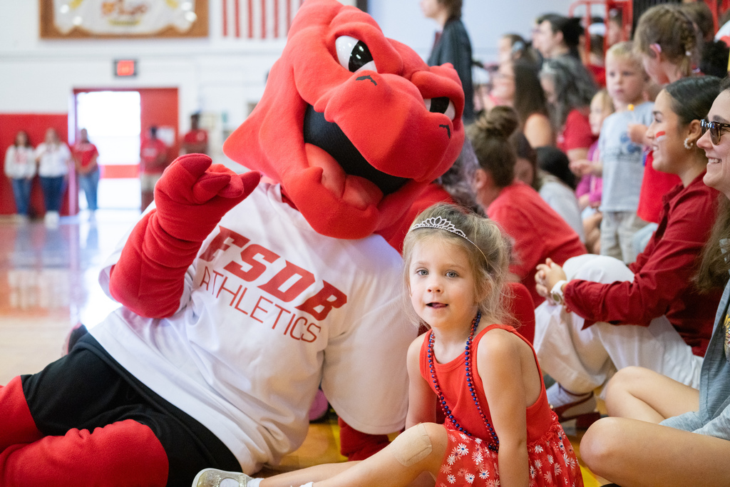 A ELC student smile with Samy the Dragon inside Settles Gym. 