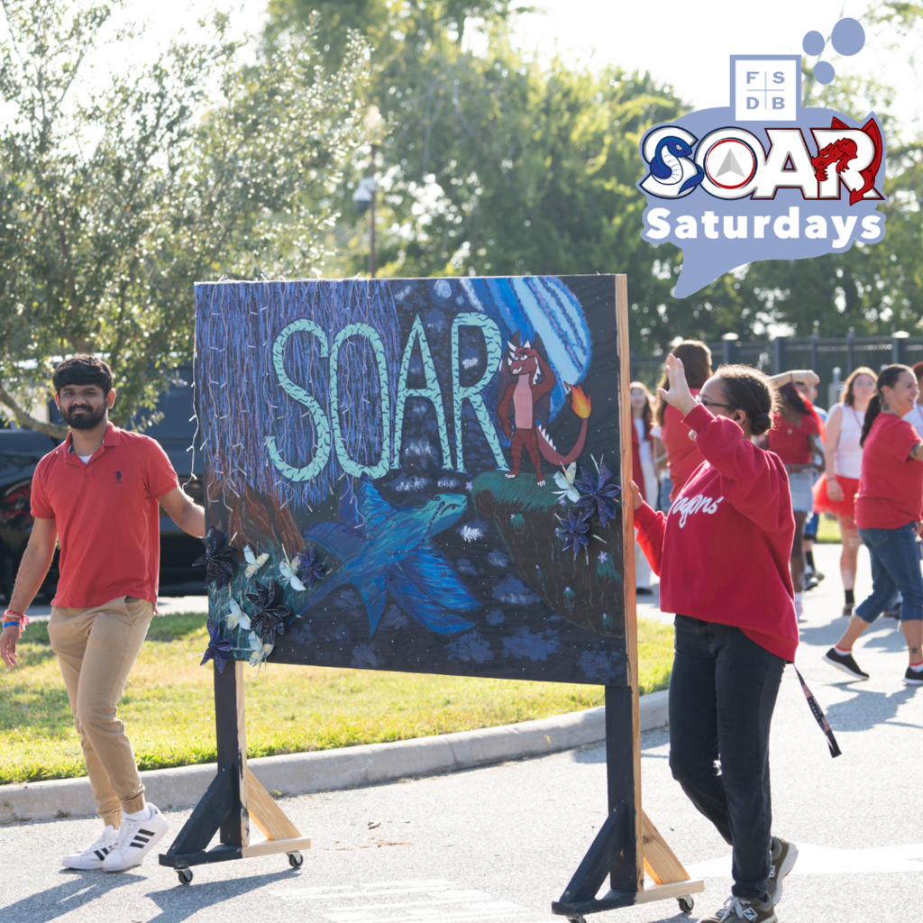 Two SOAR students wearing a red shirt walking with their banner that they created as a class during the Homecoming Parade.