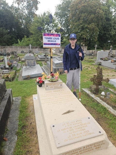Photo of Mr. Ferguson smiling for a photo with Louis Braille's grave. 