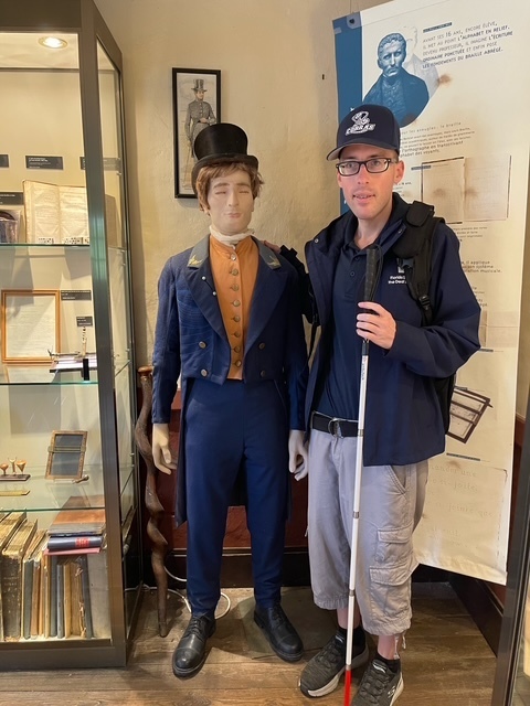 Mr. Ferguson smiling with a wax figure of Louis Braille wearing a navy suit. 