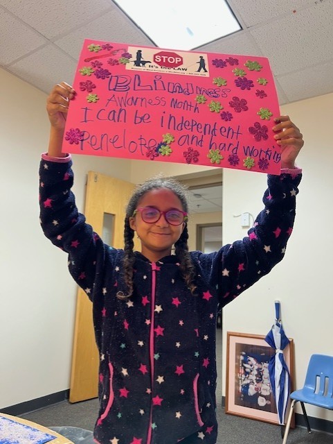 Penelopel holding a pink sign that reads, "Blindness Awareness Month–I can be independent and hard working.