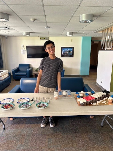 Gabe standing behind a table with cupcakes and toppings.
