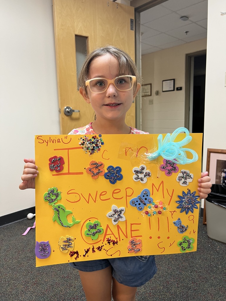 Sylvia holding a yellow sign she created that reads, "I can sweep my cane!!!"