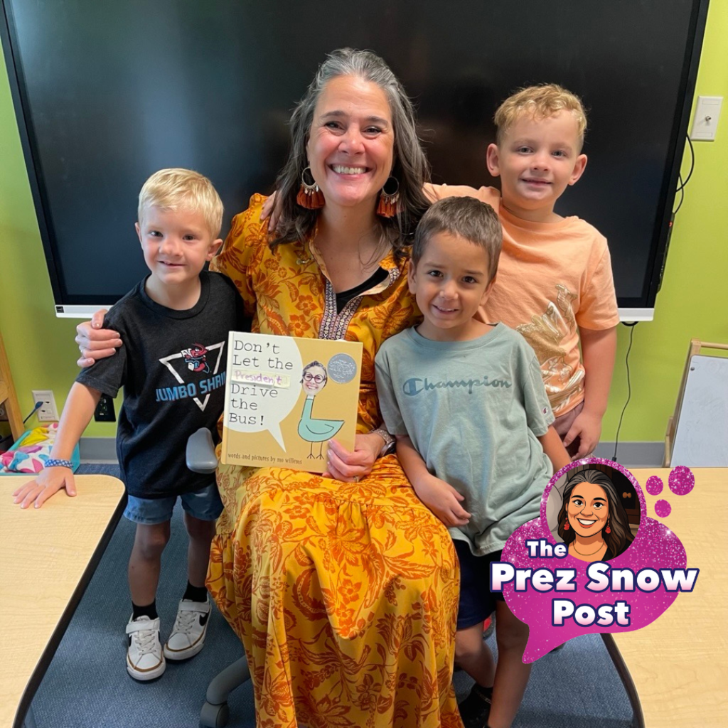 President Tracie Snow is wearing a yellow and orange dress holding the "Don't let the Piegon  drive the bus" with three deaf kindergartners in the classroom. 