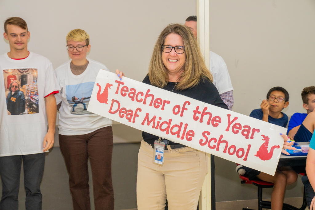 Nicole is holding the Teacher of the Year banner inside the cafeteria.