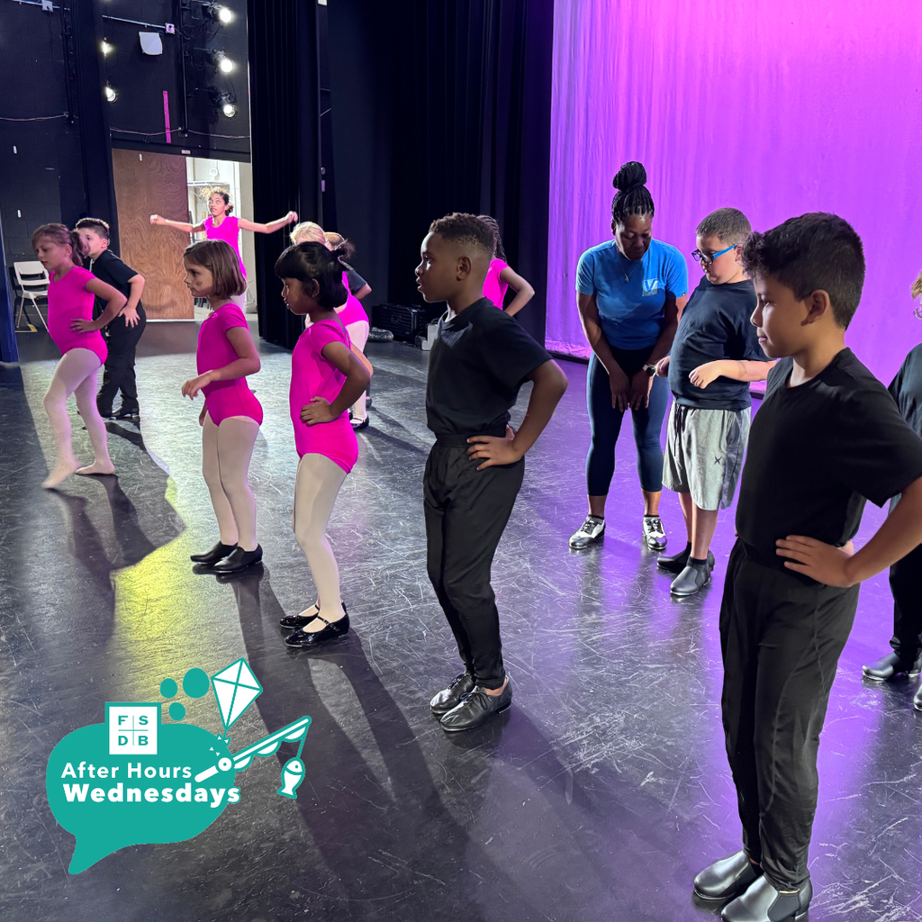 Group of elementary students on stage in their tap shoes wearing pink or black ballet clothing.
