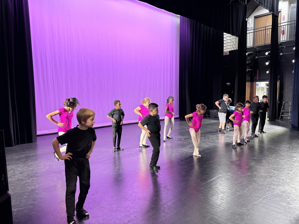 A photo of boys and girls wearing their black and pink ballet clothing practicing their dance moves on stage in Kirk.