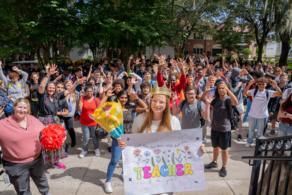 Colleen smiling with her crown, flower and sign with the whole Deaf High School Department in the background.