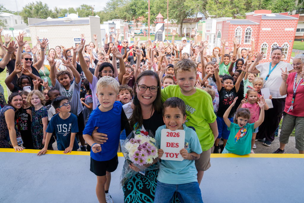 Dani is smiling with three of her students with the whole Deaf Elementary School Department behind her.