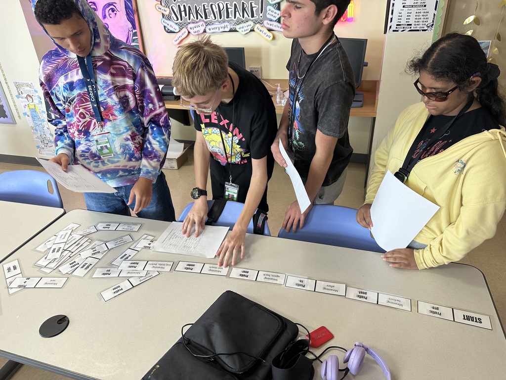 Ryan, Nicholas M, Facundo, and Danna work together reading and moving the paper dominoes (with large print and braille).