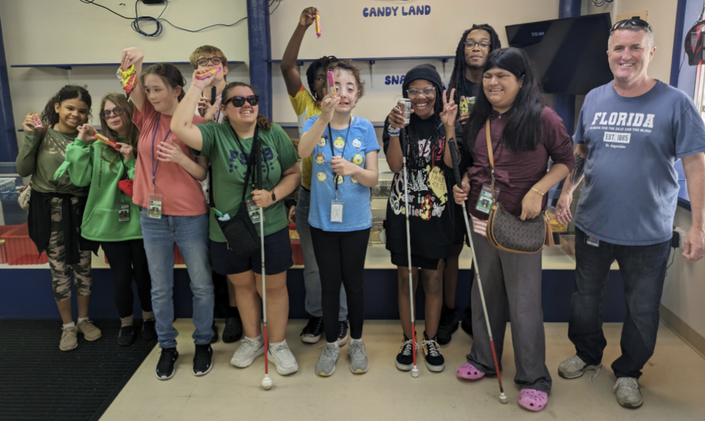 From left to right: Gabriela, Gracelynn, Kayla, Eirc, Rylee, Derrick C, Danika s, Serraya, Derrick M, Juana, and Mr. Ward. They are all smiling and several students are holding up snacks they just got.
