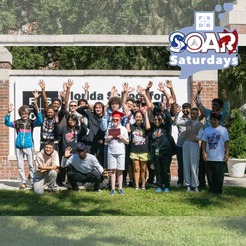 Group photo of Cassidy and her SOAR group wave their hands in the air in front of the FSDB sign. 