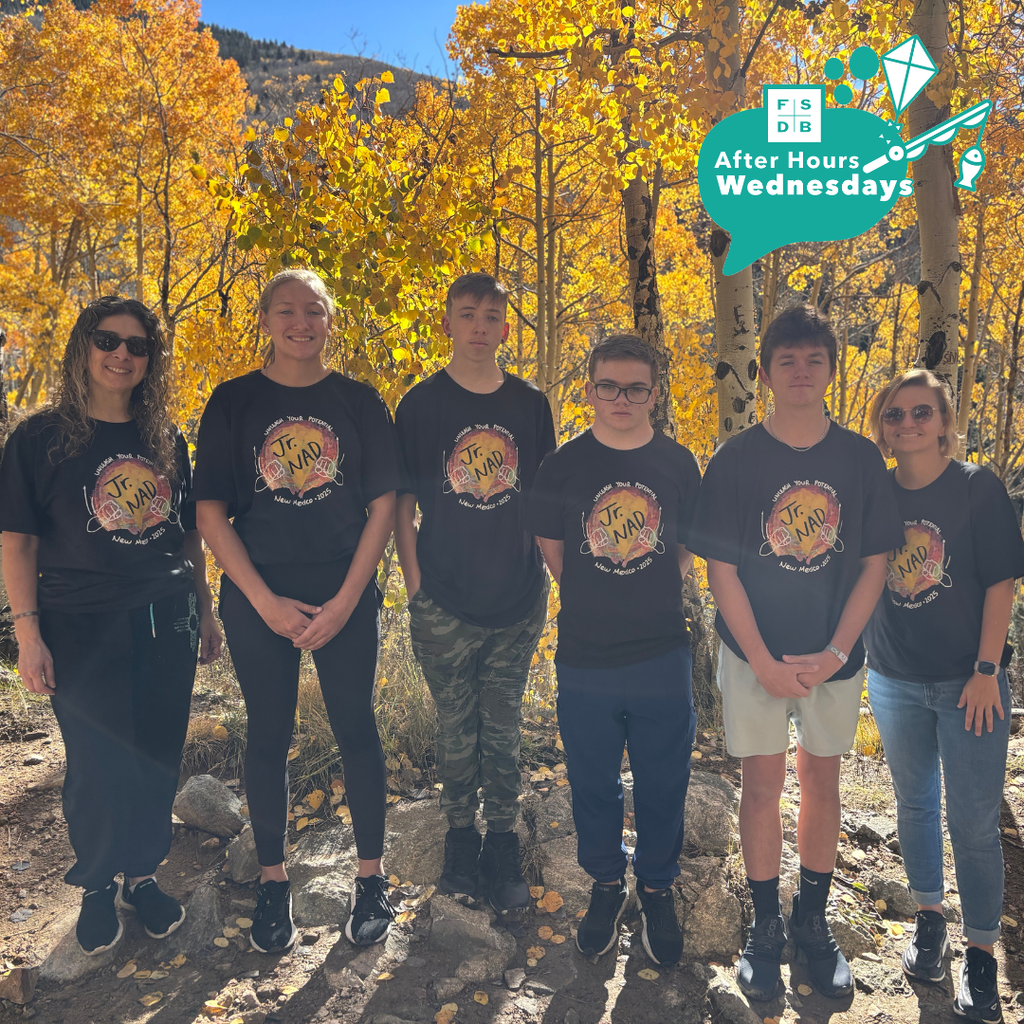 Jr. NAD group of students and staff wear matching black shirts smiling for a photo with yellow fall trees.