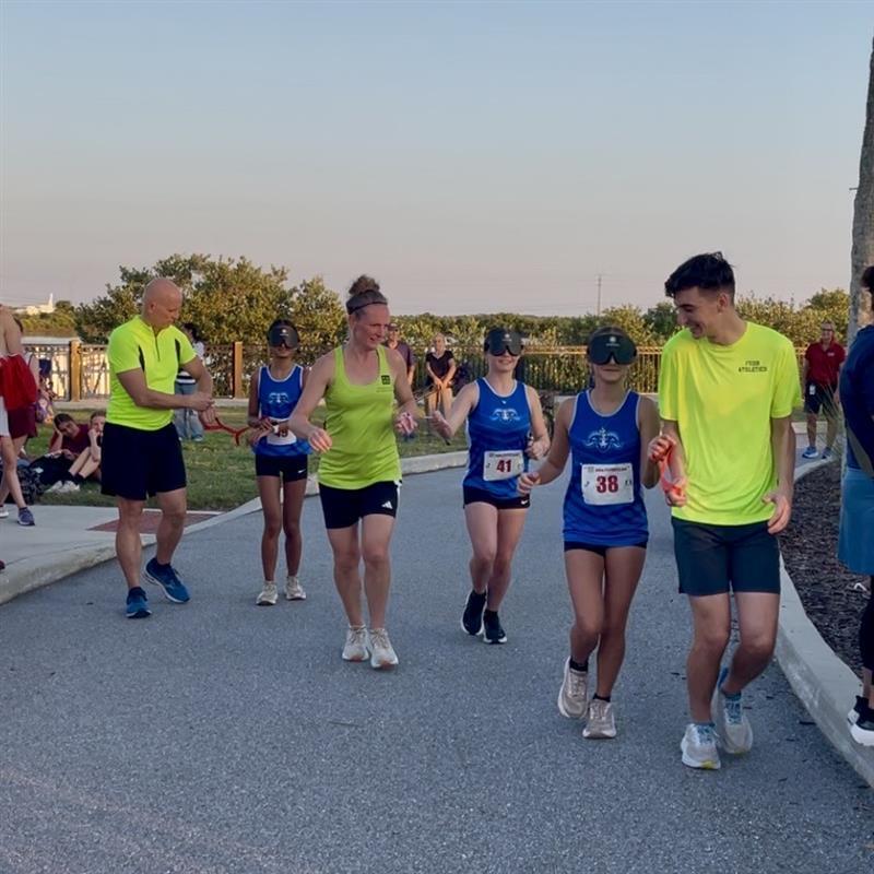 Cross Country runners hold a guide rope running with a guide on campus. 
