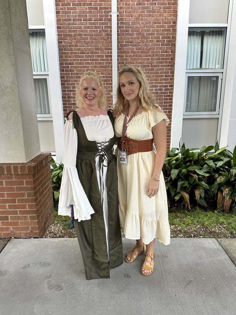 Two staff members are dressed like medieval times are smiling together outside in the walkway. 
