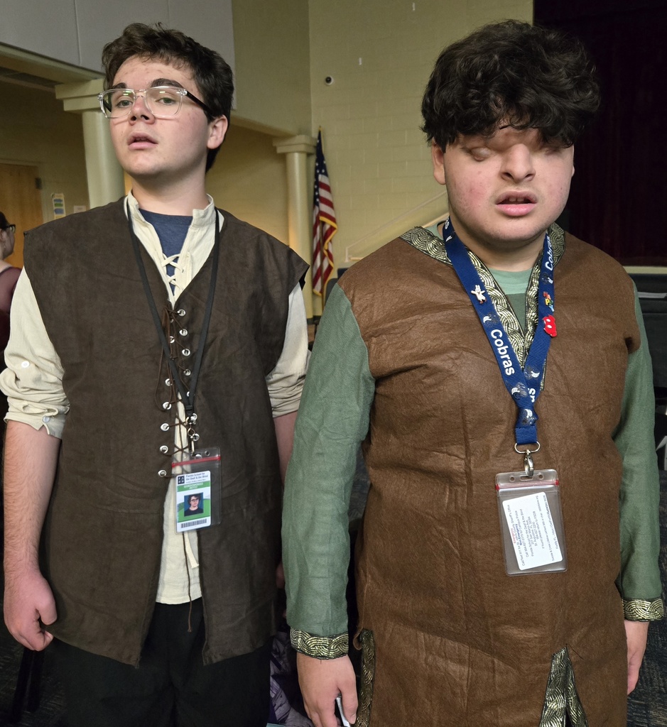 Two students are dressed like medieval times are smiling for a photo together inside the music building. 