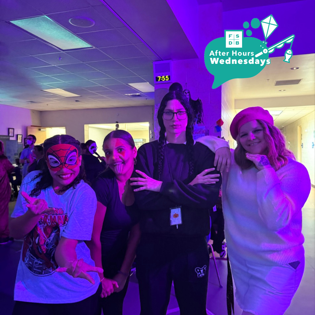 Staff and students are dressed up for halloween pose for a photo together inside the dorm with purple lights. 