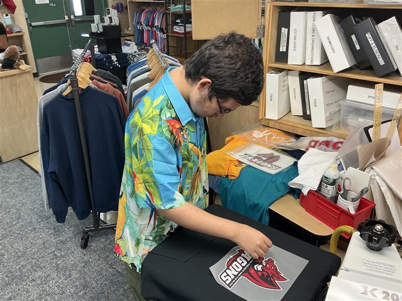 A student is working on adding the FSDB Dragons logo to a black sweatshirt inside the D&B Designs classroom. 