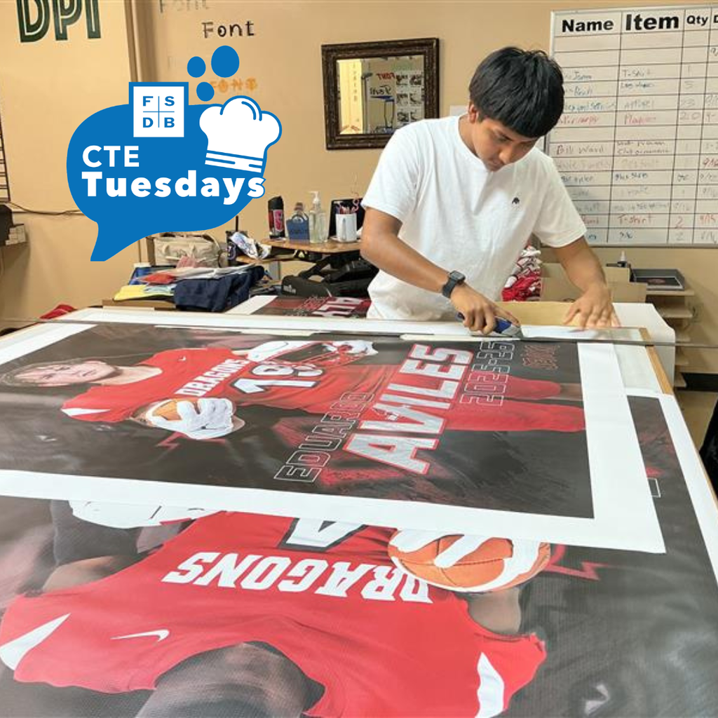 A student is working om cutting out senior posters inside D&B Designs classroom. 