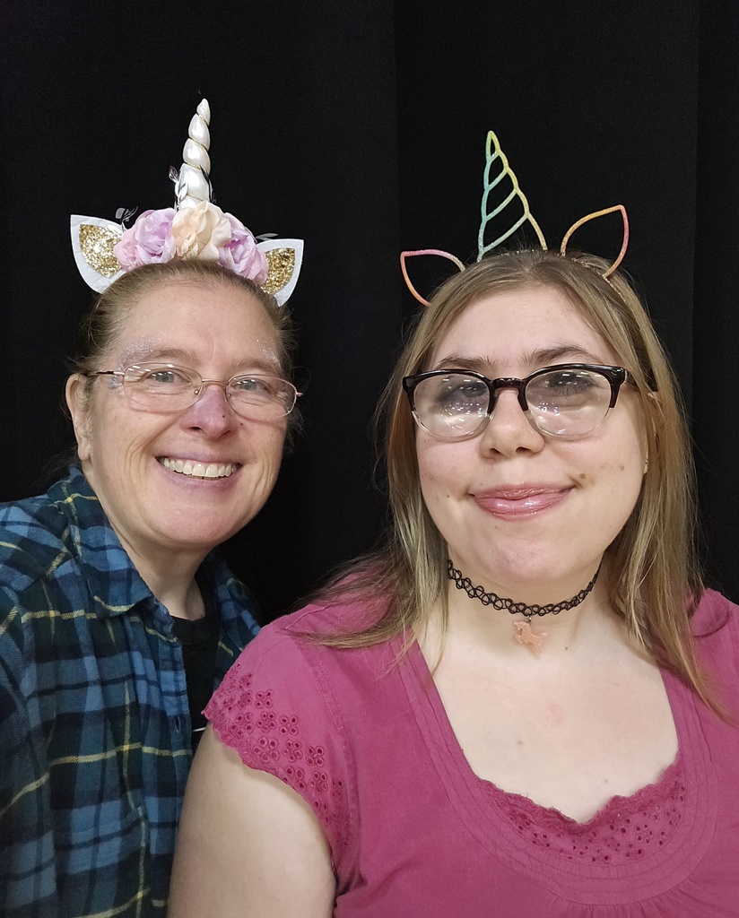 A student and staff member are wearing unicorn headbands taking a selfie together. 
