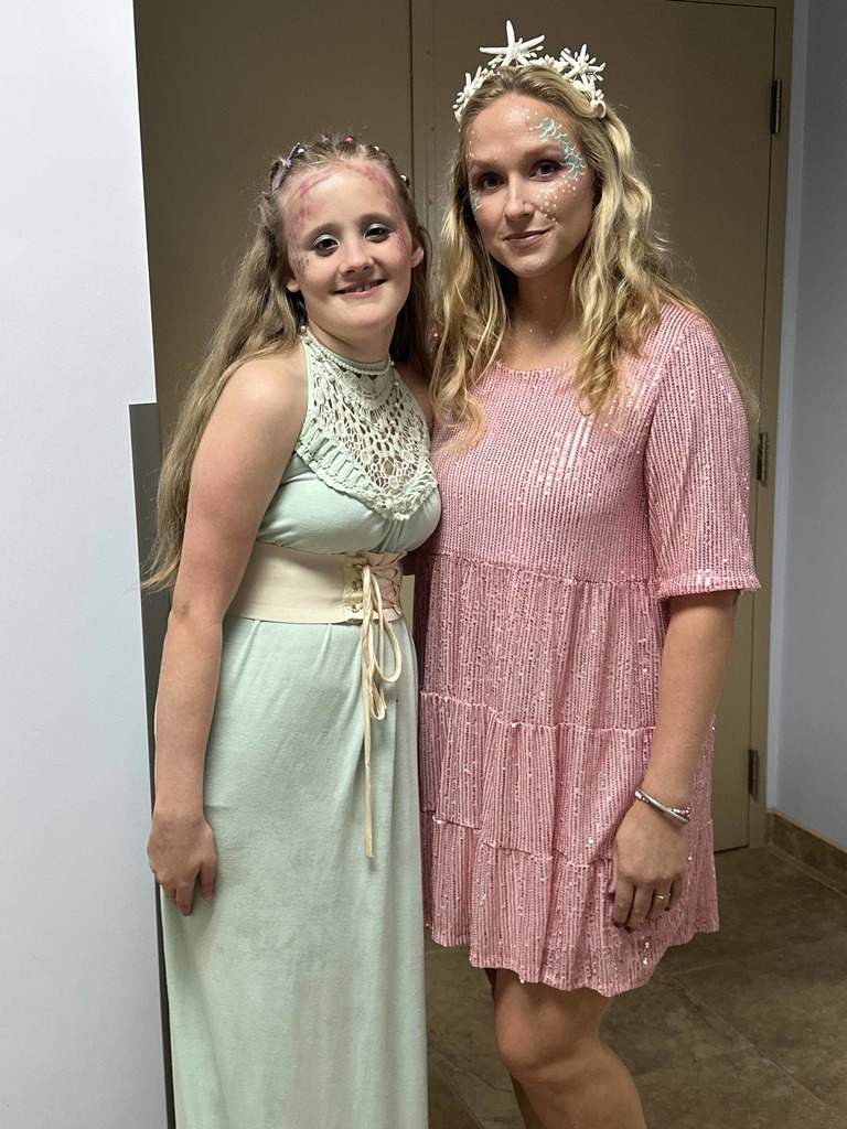 A staff member with a student dressed up mythical pose for a photo together in the hallway. 