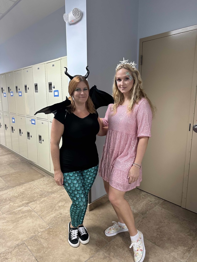 Two staff members dressed up as mythical creatures smile for a photo together inside the hallway. 