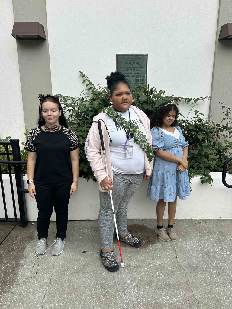 Three students all dressed up smile for a photo outside of a building. 