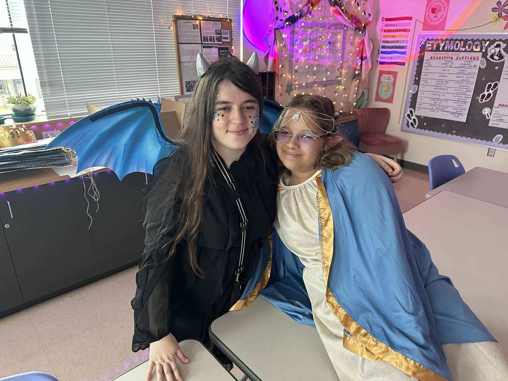 Two students dressed up as a creature and smile together for a photo inside the classroom. 