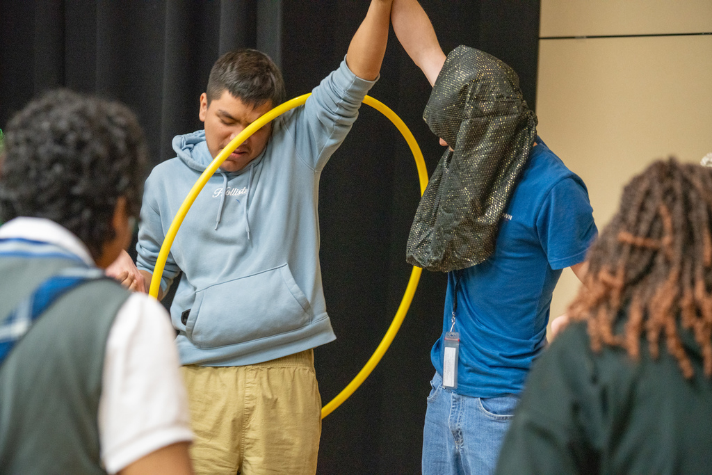 Two students hold hands and working together as a team to get through the hula hoop. 
