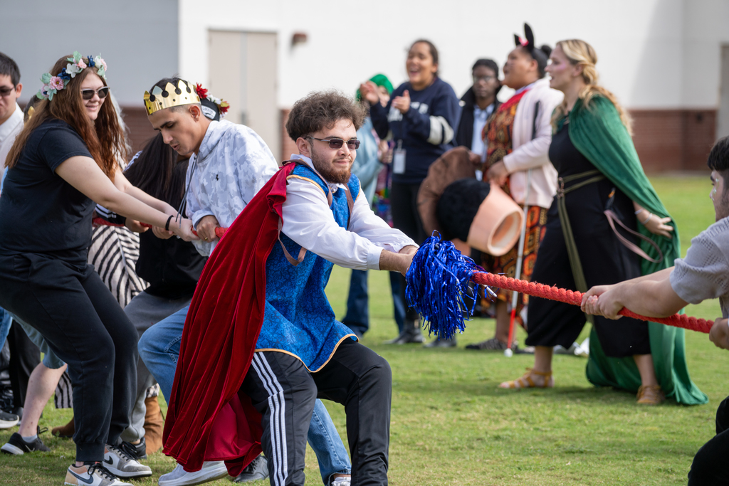 A student is the leader of the group is pulling the rope outside on the football practice field. 