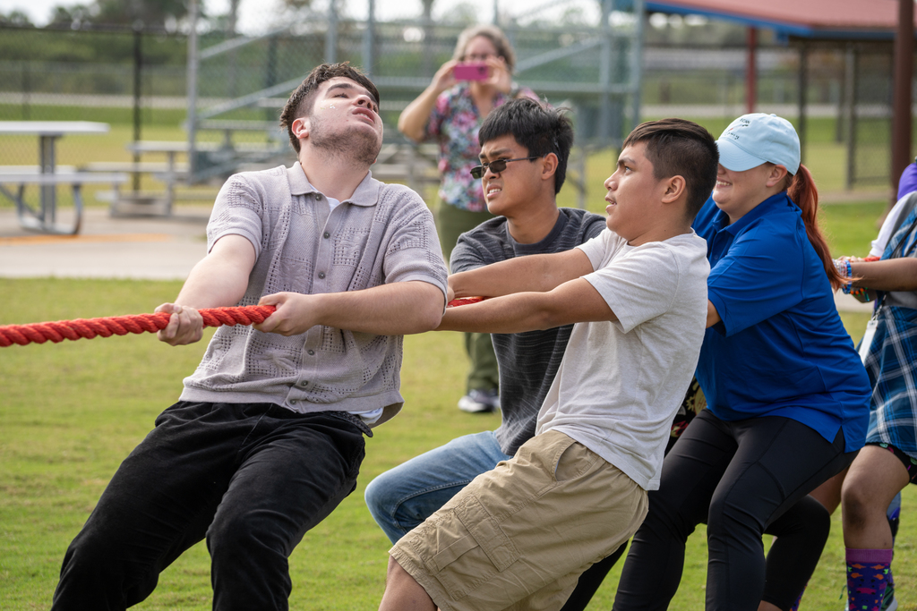 A bunch of students working hard and pulling on the ropes during tug of war outside. 
