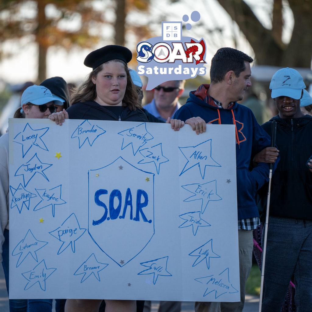 A SOAR student holding a white board with stars of each SOAR student name walking outside during the Homecoming Parade. 