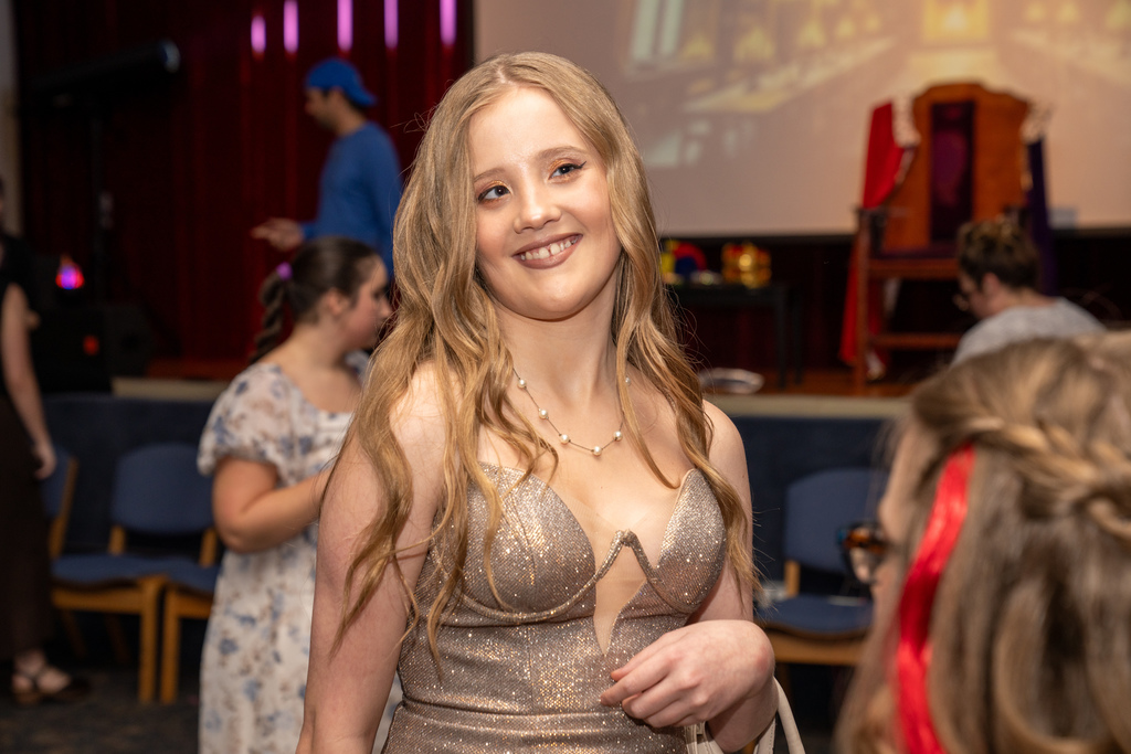 A student dressed in rose gold dress smile for her photo inside the music building. 