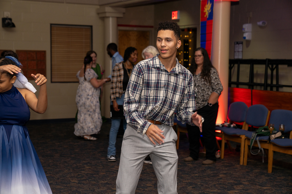 A student wearing a plaid shirt is smiling and dancing on the dance floor in the music building. 